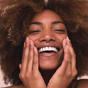 Photo of a happy woman with her hands at her face. Click ate the photo for information about discovering your skin type. 